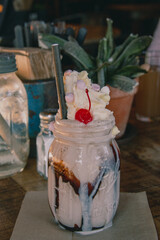 Fototapeta na wymiar Messy milkshake served in a jar with whipped cream and cherry in rustic setting
