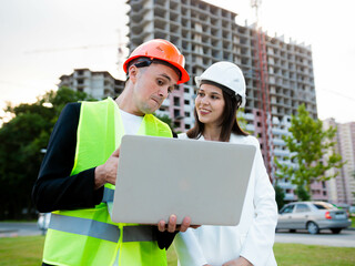 Construction professionals use a laptop computer at a construction site. Real estate construction project with civil engineer, architectural investor. Business woman and worker discuss plan details
