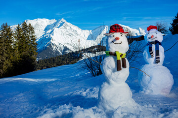 Two snowmen build with carrot hat and scarf over mountains