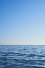 Obraz premium Dark blue water from the sea with blue sky. Light comes from the right. Vertical format, also suitable as a poster or background. Free space for text or objects. 