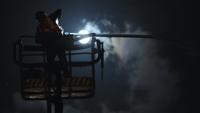 silhouette of a electric engineer working on a street lamp with the moon in the background