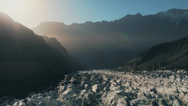 Glacier duringAERIAL 4K, drone flights quite close to the surface of a white glacier crossing it, looks into the end of the glacier and light rays from the sunrise,, Passu, Pakistan