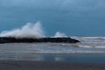 Big waves crashing against the breakwater of the beach of El Puerto de Sagunto on a stormy day under a dramatic sky. Port of Sagunt - Valencia