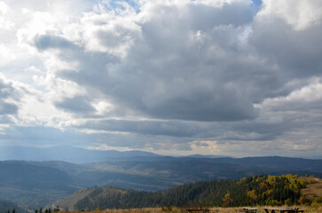 The sun's rays shine through the clouds over the picturesque mountains covered with colorful forests. Autumn landscape in the Carpathians, Ukraine