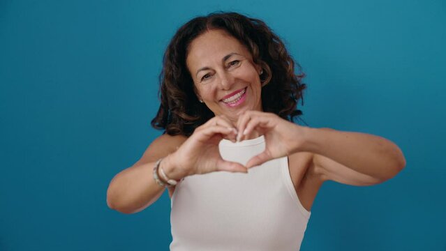 Middle age woman smiling confident doing heart gesture with hands over isolated blue background