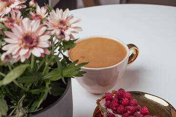 View to blurred white cup with delicious coffee on white background. Beautiful pink chrysanthemums in pot in the foreground. Place for your text.