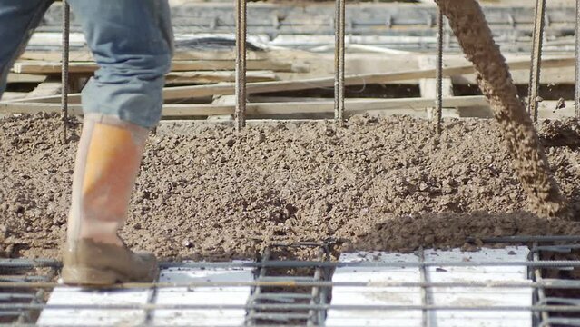 Construction worker controls the flow of concrete mix. Before mixture can be poured, forms need to be built to hold concrete in place. Laborer pulls large hose of concrete pumping machine for concreti