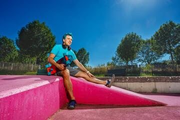 Portrait of an adult man with blue hair sit holding skateboard