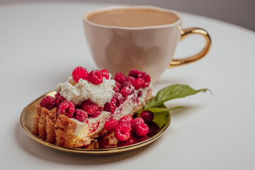 Delicious piece of cake with fresh raspberries and blurred cup of aromatic coffee in background. Blurred white background. Sweet concept. Excellent image for dessert banners and advertisements.