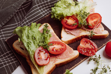 Close-up of delicious toasts decorated with microgreens and tomatoes and fresh lettuce. Healthy breakfast. Green towel in background. White background.	