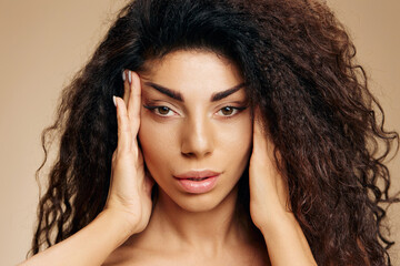 LIFTING SKIN CONCEPT. Pretty sexy adorable beautiful awesome curly Latin lady touch temples pull facial skin massage head posing isolated on pastel beige background, look at camera. Copy space banner