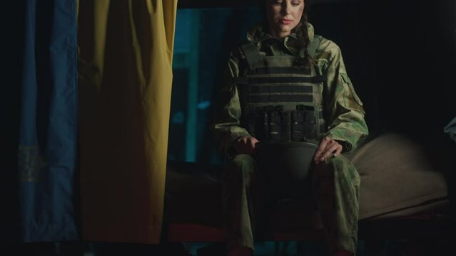 Ukrainian female soldier in a dugout with a Ukrainian flag puts on a helmet in anticipation of an attack by Russian invaders - Ukrainian war concept. 