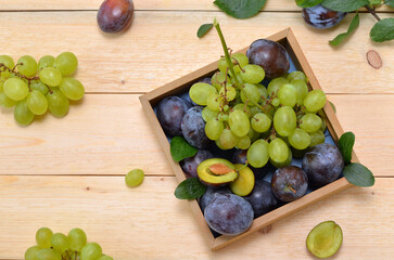 purple plums and green grapes harvest in a box on a wooden background, flat lay