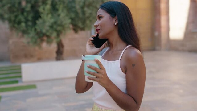 Young beautiful woman talking on smartphone drinking coffee at street
