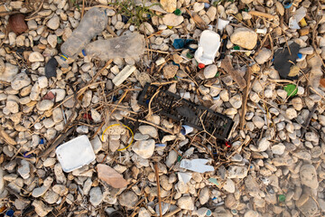 Plastic garbage on the seashore. Top view of a polluted beach. Stones and shells mixed with plastic. Environment concept