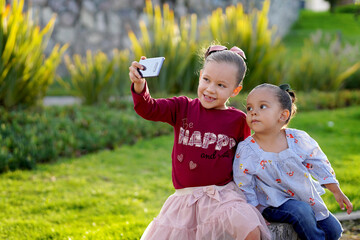 Niñas hermosas felices tomándose una foto selfie posando sentadas en un jardín parque al aire...