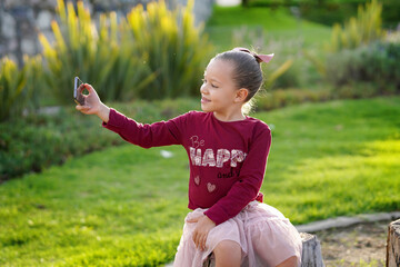 Niña hermosa feliz tomándose una foto selfie posando sentada en un jardín parque al aire libre...