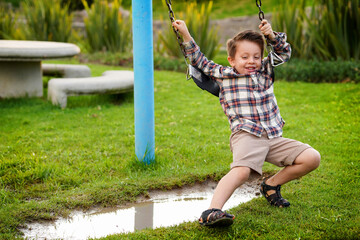 Niño feliz en el parque en el columpio jugando divertido colgado arriba de un charco de agua lleno...