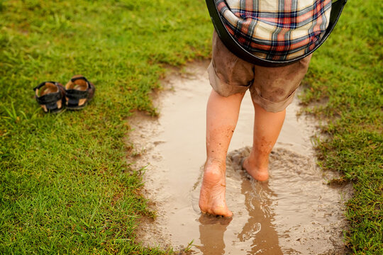 Niño feliz jugando a columpiarse en el parque al aire libre mojando sus pies en el lodo en un charco de agua por la lluvia