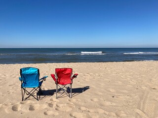 A blue and a red chair standing empty on the beach of the North Sea under a blue sky