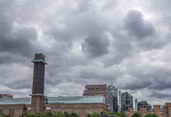 Fototapeta na wymiar London, England, UK - July 6, 2022: From Thames River. On south shore, Tate modern art museum under heavy cloudscape with its tower and glass upper level