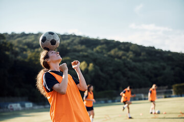 Skillful female soccer player balancing ball on head on playing field.