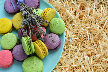 Top view of colorful macaroons on blue plate, decorated with lavender flowers, placed on decorative...