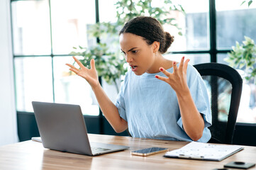 Irritated angry young mixed race business lady, company director, supervisor, annoyed looking at...