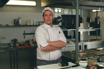 Naklejka na ściany i meble Portrait of handsome male chef in uniform standing on kitchen of restaurant