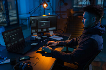 cybercrime, hacking and technology concept - male hacker in dark room writing code or using computer virus program for cyber attack