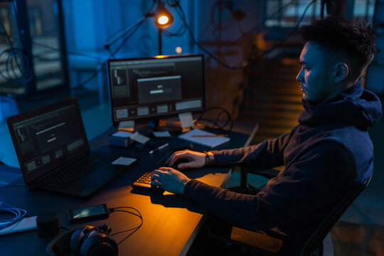 cybercrime, hacking and technology concept - male hacker in dark room writing code or using computer virus program for cyber attack