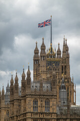 Fototapeta na wymiar London, England, UK - July 6, 2022: From Thames River. Victoria Tower with flag on top and golden trims over Westminster palace and hall under gray cloudscape.