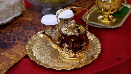Golden teapot and golden tray on table with red cloth 
