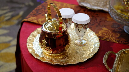 Golden teapot and golden tray on table with red cloth 