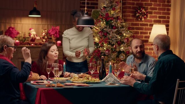 Festive african american woman bringing main course to table while people enjoying Christmas dinner. Joyful family members celebrating winter feast with traditional home cooked food.