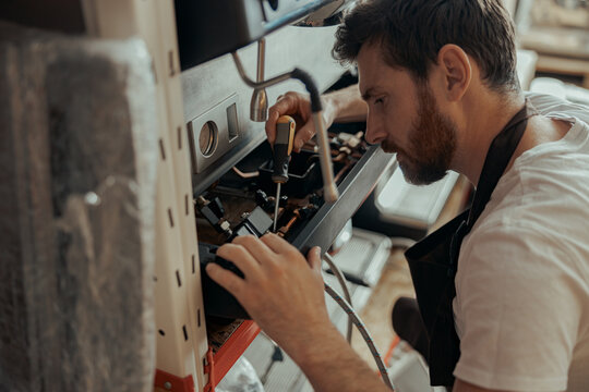 Handsome worker in uniform repairing coffee machine in a workshop - Powered by Adobe