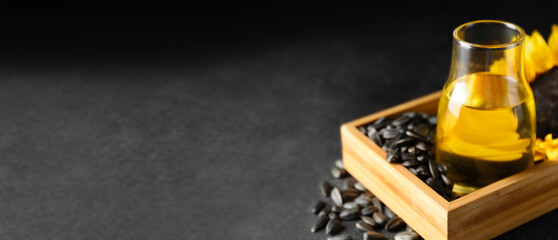Glass bottle of sunflower oil and seeds on dark background with space for text