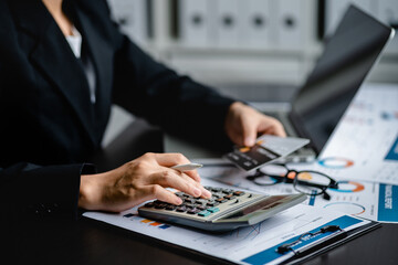 Businesswomen or Accountants use a calculator to doing income-expense accounting and analyze company financial reports. investment, balance sheets, taxes, planning and business strategies concept. - obrazy, fototapety, plakaty