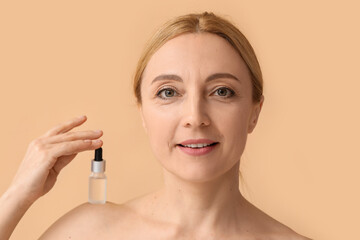 Mature woman with cosmetic serum on beige background