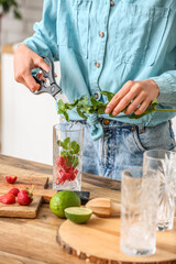 Woman adding fresh mint into glass with strawberry lemonade in kitchen