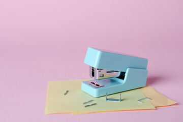 Stapler with sticky notes and staples on pink background