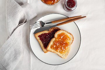 Plate of delicious toasts with jam and cutlery on light table