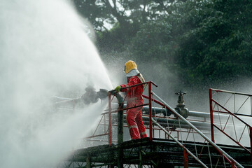 Fototapeta premium Firefighter try to extinguish or get rid of fire from gas pipe on top of building and he protect themselves by using water curtain.
