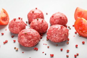Raw meat balls with peppercorns and tomato slices on light background