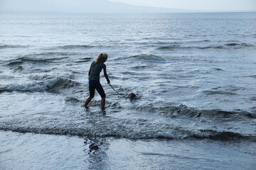 A woman playing with the dog at the beach .