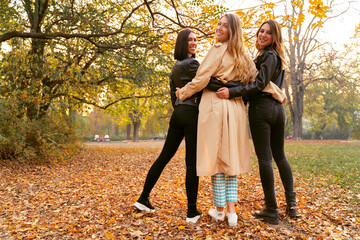 Group of attractive girls hugging in beautiful autumn season park, back turned towards camera 
