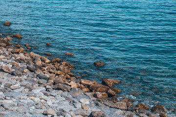 The stone shore is washed by the turquoise sea. The waves of the ocean on a stone shore.
