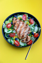 grilled chicken salad on black plate honey mustard sauce, yellow background with copy space	