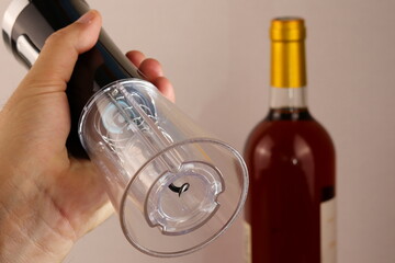 A rechargeable electric corkscrew in the hand of a person to open a bottle of wine in the background