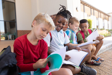 Multiracial elementary schoolboys studying through books while sitting on floor at school